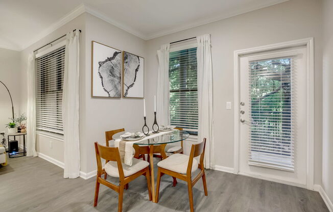 A dining room with a table set for two and a plant on the side table.