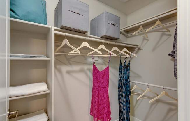 a walk in closet with a pink dress and white hangers