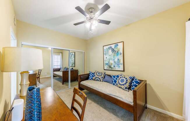 A bedroom with a bed, a chair, a table, and a ceiling fan.