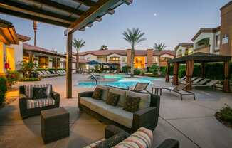 a patio with couches and chairs around a pool at night