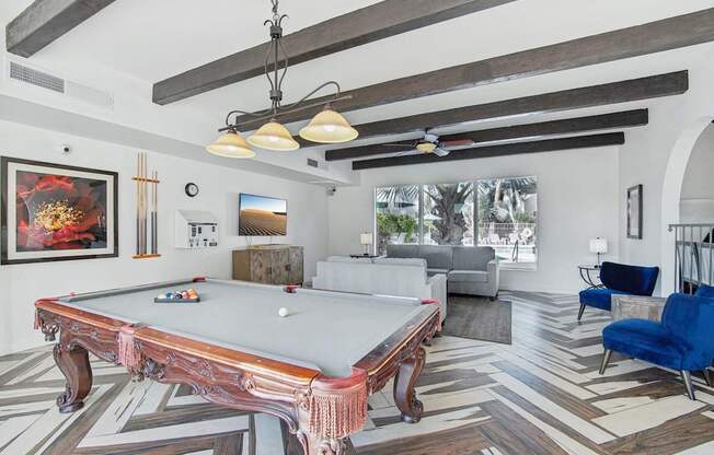 A pool table is in the middle of a room with a blue chair to the right.