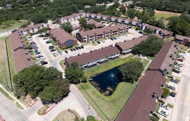 A bird's eye view of a residential complex with a pond in the middle.