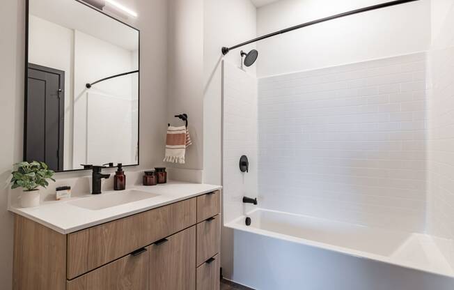 Bloomington, MN Apartments Near Mall of America - Carbon31 - Modern Bathroom with White Walls, Shower and Bathtub Combo, Sink, White Countertop, Black Plumbing Fixtures, and Large Mirror