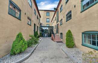 A long, narrow alleyway between two tan buildings with green trim and steps leading to the entrance.