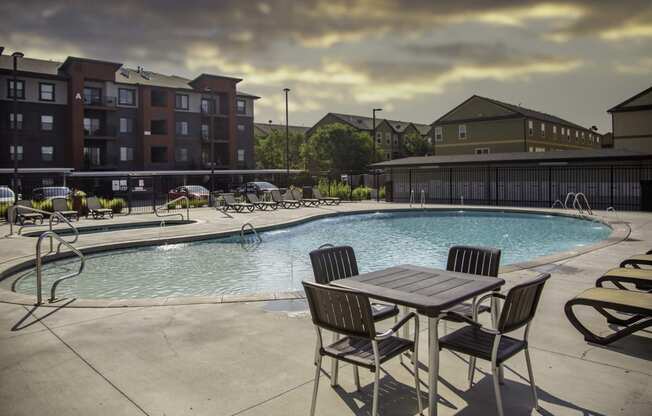 a swimming pool with a table and chairs and a building in the background