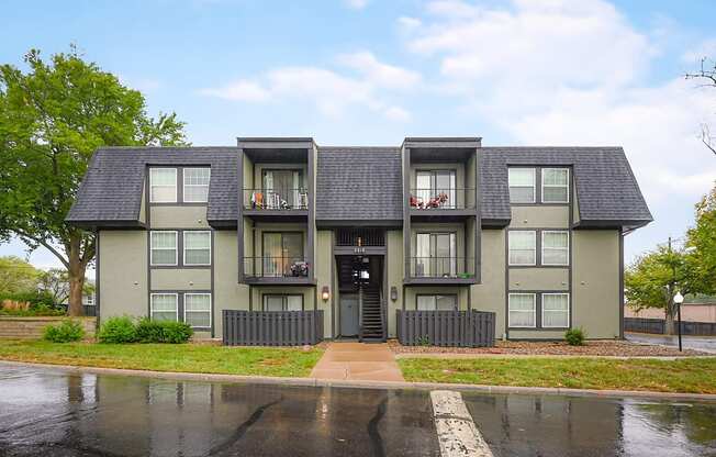 A grey apartment building with a black door and windows.