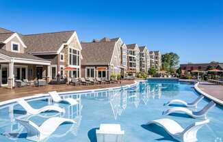 a large swimming pool with white chairs in front of apartment buildings