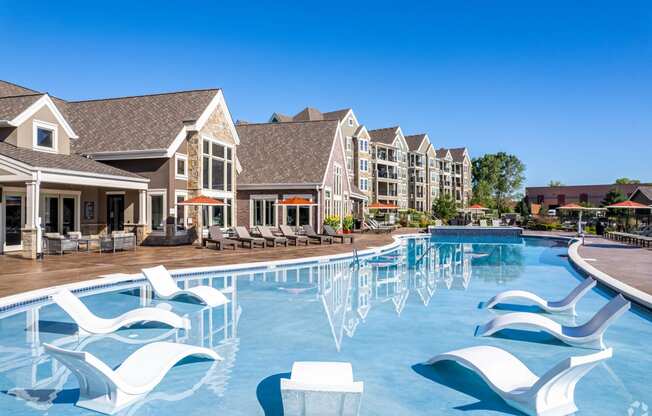 a large swimming pool with white chairs in front of apartment buildings