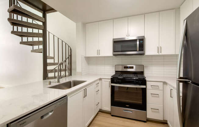 A modern kitchen with a stainless steel refrigerator, a microwave above the stove, and a spiral staircase.