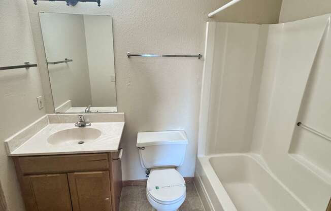 A white toilet sits in a bathroom next to a sink and a bathtub.