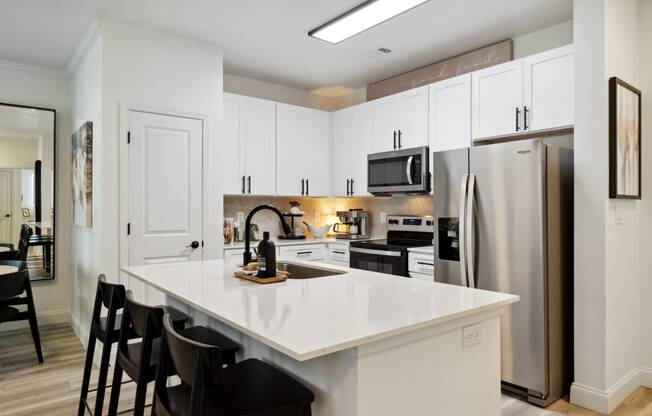 a kitchen with white cabinets and a large white island with black stools