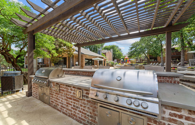 A large outdoor grill is under a pergola in a backyard.
