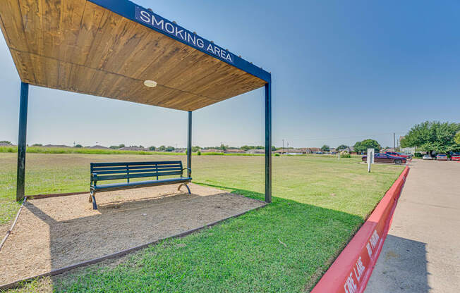 A smoking area with a bench under a wooden canopy.