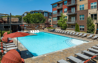 a swimming pool with chairs and umbrellas in front of an apartment building