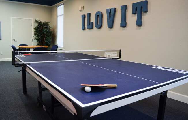 a blue ping pong table in a room with a scoreboard on the wall