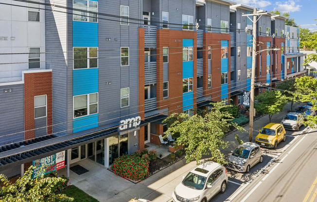 A street view of a row of apartment buildings with cars parked on the street.