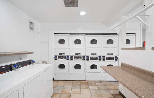 a laundry room with white cabinets and a row of white washing machines