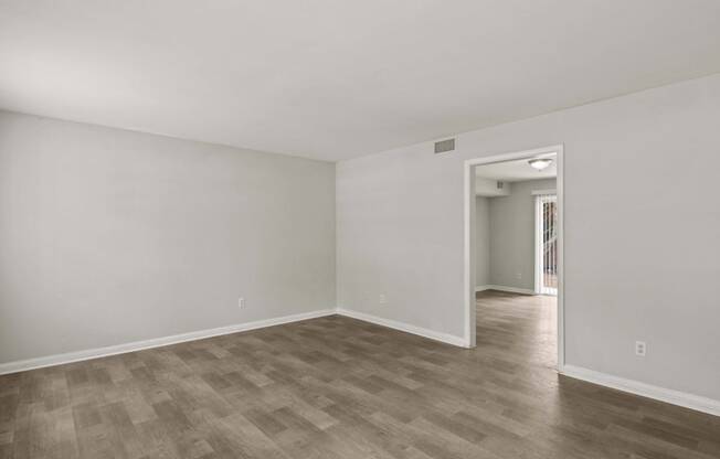 the living room of an apartment with white walls and wood flooring