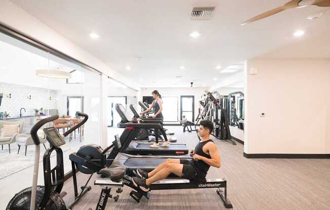 A man is working out on a rowing machine in a spacious gym.