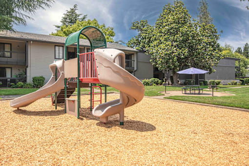 A playground with a picnic table and umbrella nearby