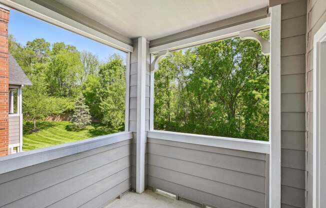 A sunny day with a view of a green lawn and trees from a covered porch.