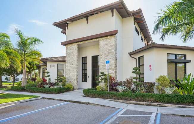 A building with a white facade and a brown roof is surrounded by greenery.