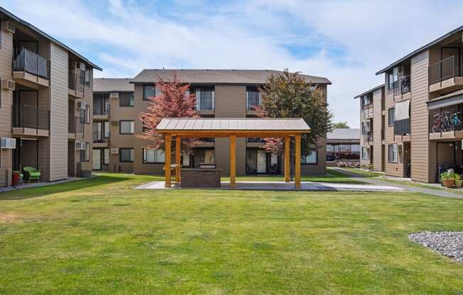 The Brix community courtyard surrounded by grass, trees, and apartments with a covered structure for residents in the center. at Brix, Washington, 99362