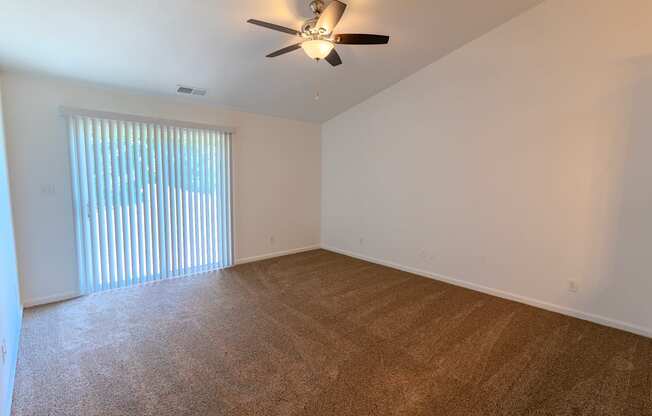 an empty living room with a large window and a ceiling fan