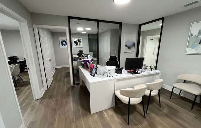 A room with a desk and chairs with a mirror on the wall.