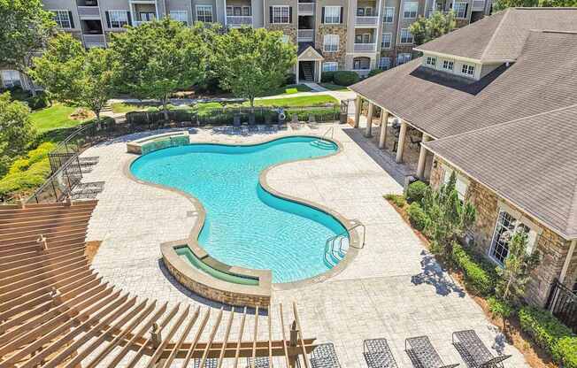 A large swimming pool surrounded by a wooden deck and lounge chairs.