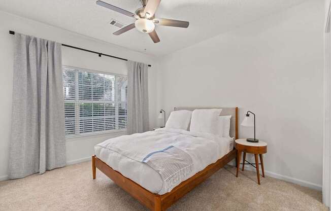 A bedroom with a bed, a small table, and a ceiling fan.