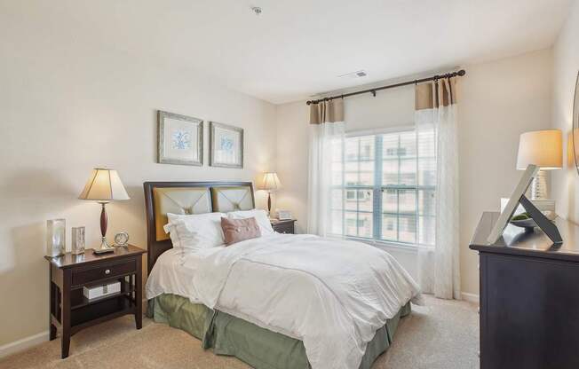 A bedroom with a large bed, two lamps, and a window with curtains.