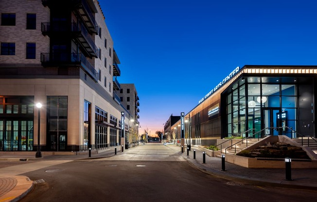 A city street at dusk with buildings on either side and a clear sky.