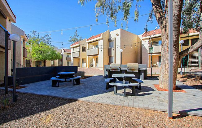 a courtyard with picnic tables and benches and buildings in the background