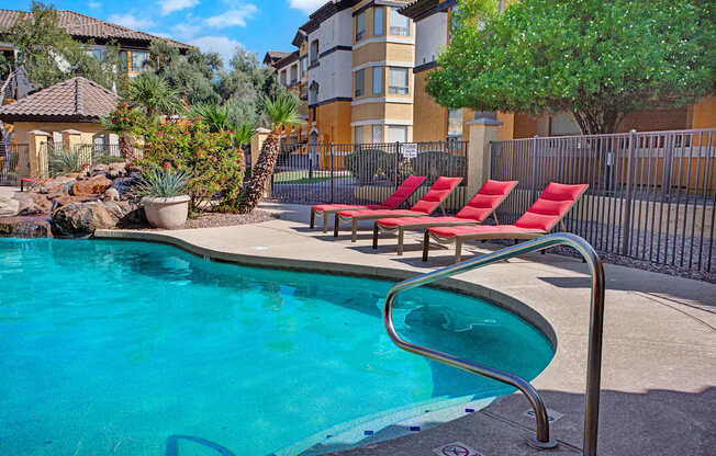 A pool with a metal railing and red chairs.