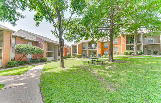A grassy area with a bench and trees in front of apartment buildings at Copper Hill Apartments, Bedford
