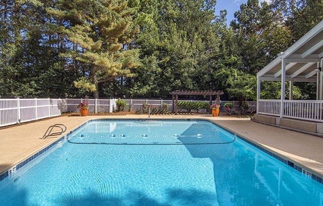 A blue swimming pool surrounded by a white fence and trees.