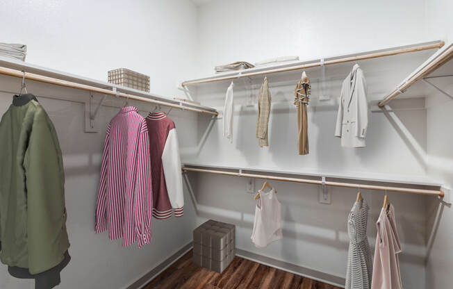 A white closet with clothes hanging on shelves and hangers.