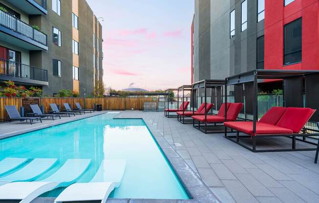 A swimming pool surrounded by red lounge chairs.