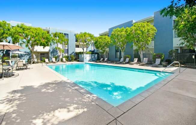 a swimming pool in front of a building with chairs and trees