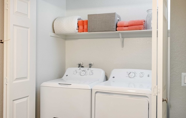 a white washer and dryer in a white laundry room with a shelf above