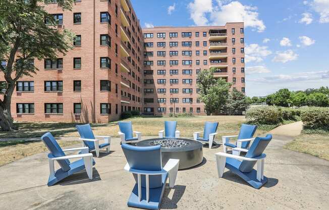 an outdoor patio with blue chairs and a fire pit in front of an apartment building