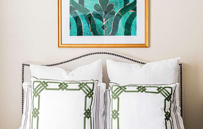 a bedroom with white bedding and a turquoise painting hanging above the bed