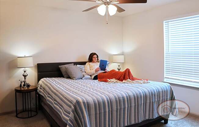 A woman is sitting on a bed looking on an IPad.