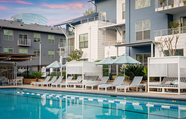 A swimming pool with sun loungers and umbrellas in front of apartment buildings.