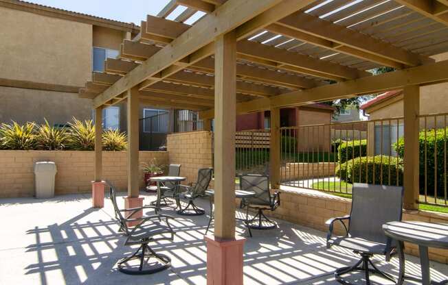 a patio with tables and chairs under a wooden canopy