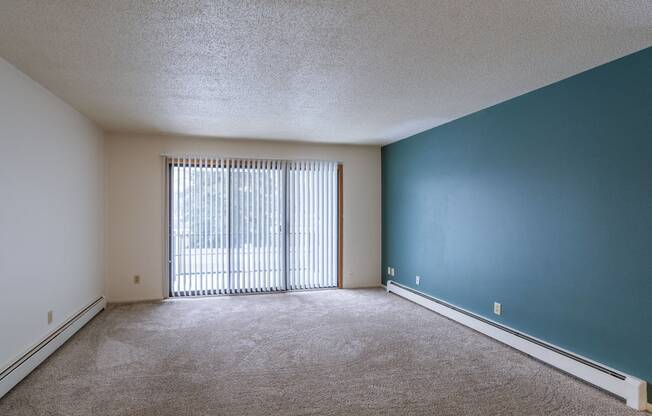 an empty living room with a large window and a blue wall. Fargo, ND Betty Ann Apartments