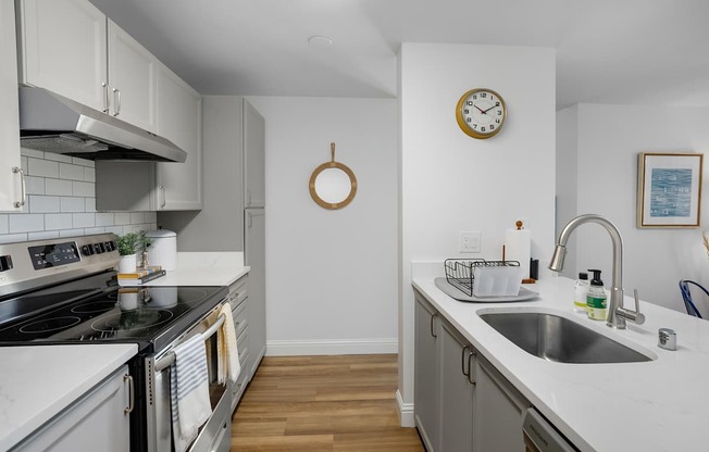 A kitchen with a stove, sink, and clock on the wall.