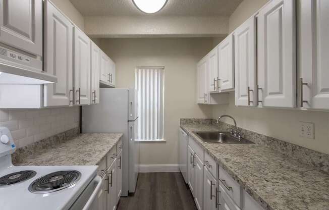 A kitchen with white cabinets and white appliances in a 2 bedroom, 2 bath with balcony apartment home at Harvard Square Apartments in the Vickery Midtown neighborhood of Dallas, TX.