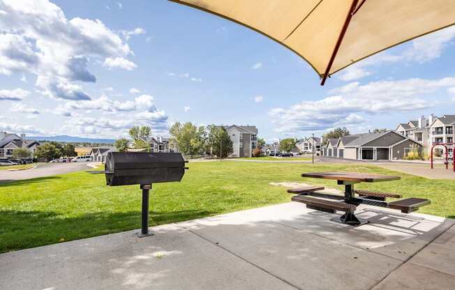 A black mailbox sits on a sidewalk next to a picnic table under a yellow canopy.